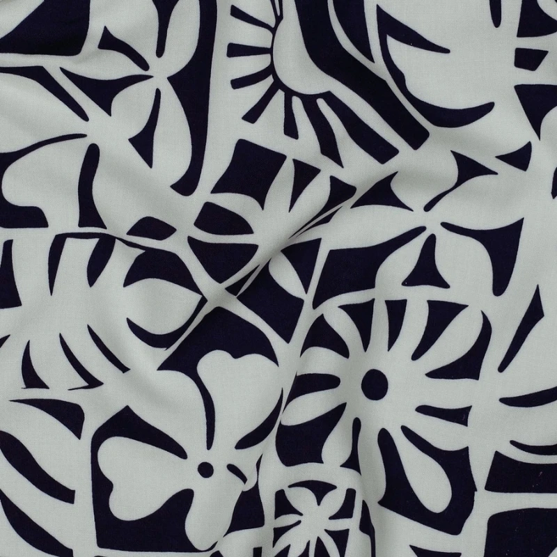 tela de viscosa 100 % Ecovero™ doblada mostrando el derecho y el revés del tejido, con un original estampado de estilo tropical en azul marino y blanco que incluye hojas de monstera y motivos solares.